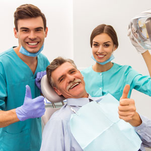 Young doctor dentist and elderly patient showing thumb up with assistant