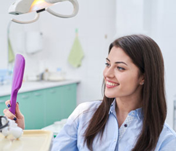 A woman sitting in a dental chair at dental clinic smiling looking at a mirror