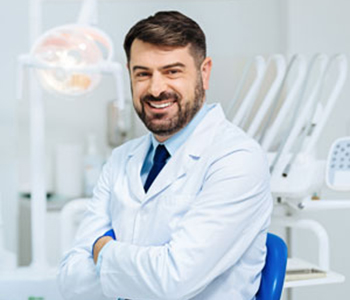 Positive bearded dentist smiling with arms crossed