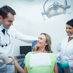 Male dentist with assistant shaking hands with woman in the dentists chair