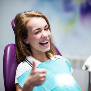 Cured woman patient giving thumbs up and smiling in the dental office
