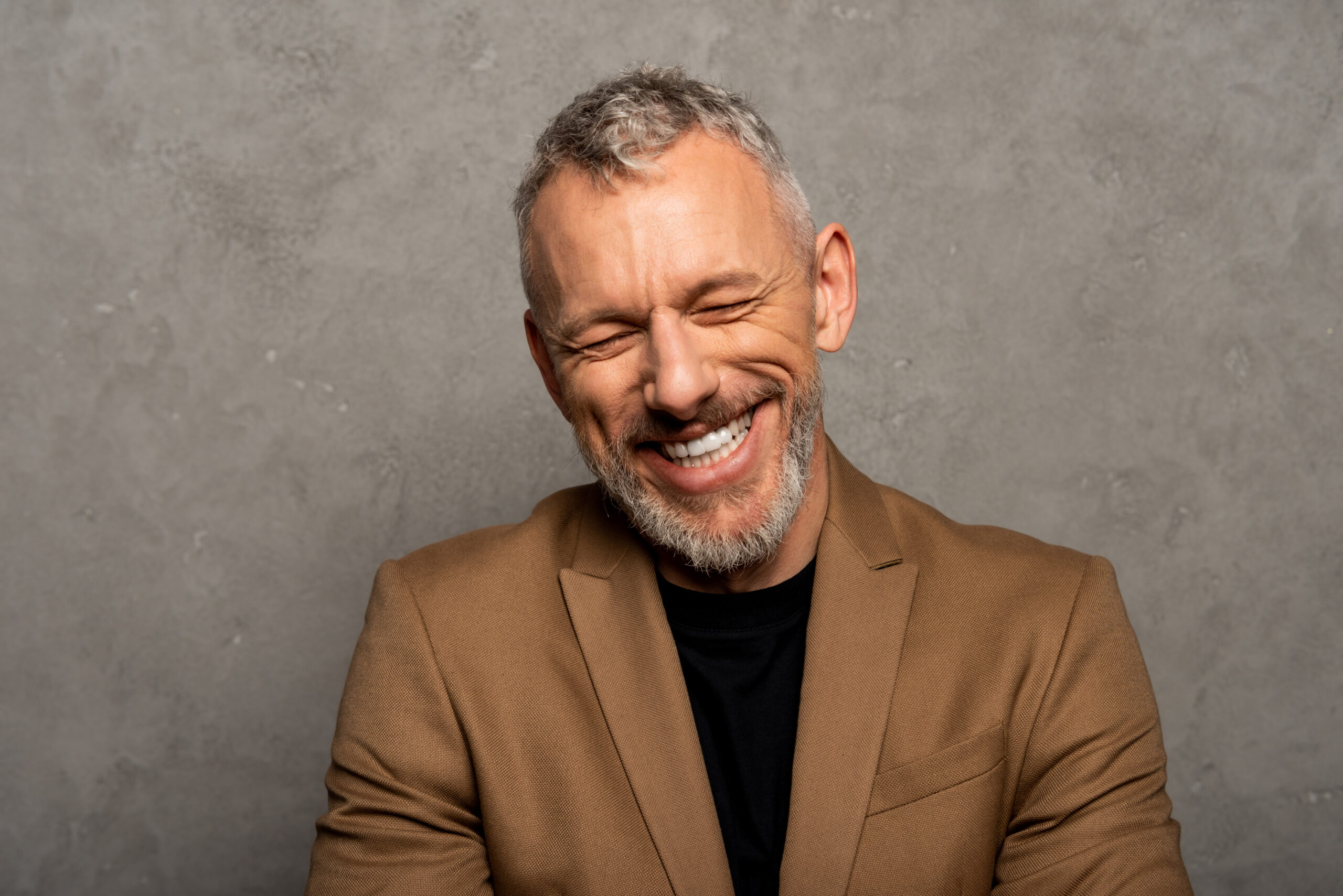 cheerful man with closed eyes laughing on grey